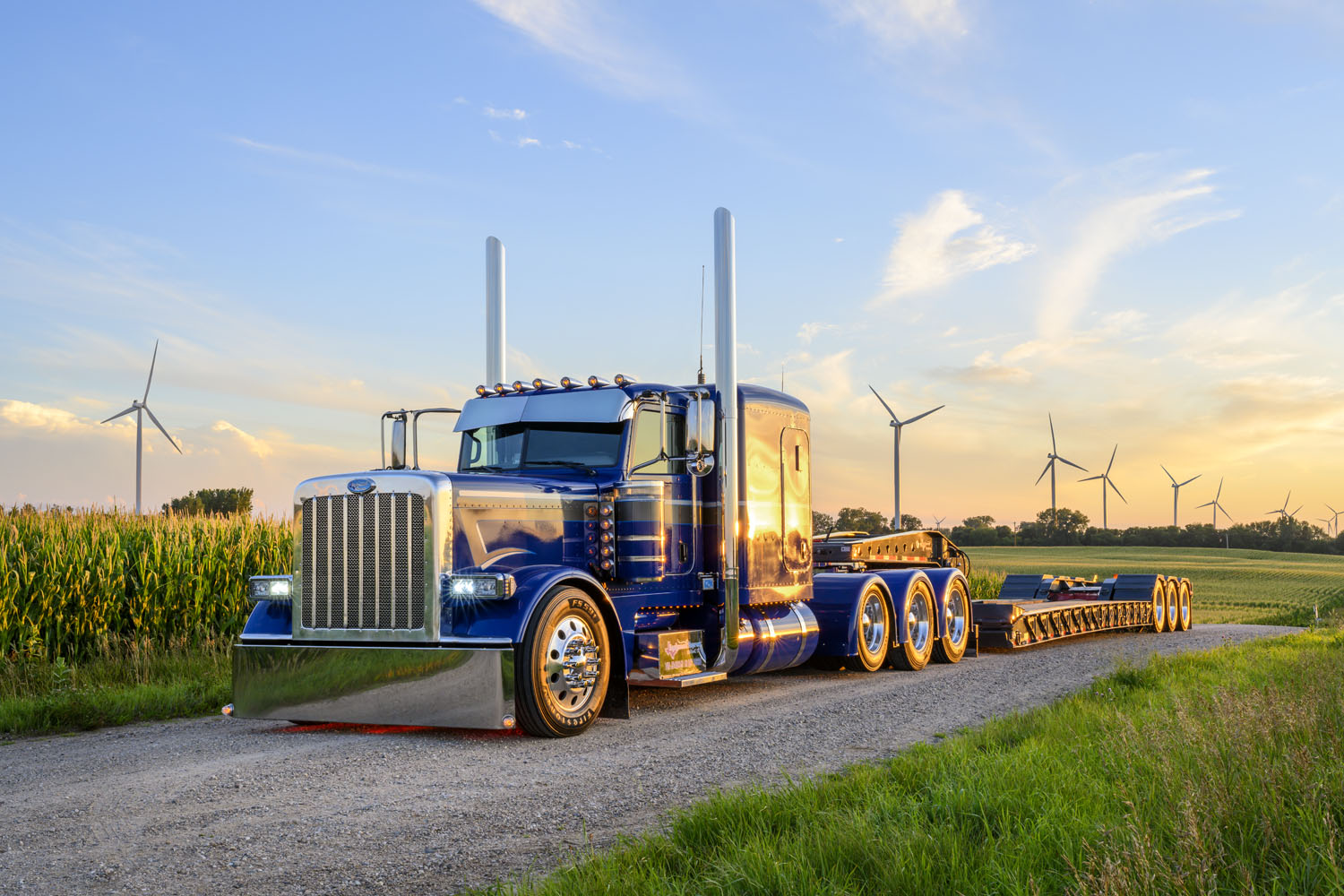 Blue commercial truck against background of corn and wind turbines.
